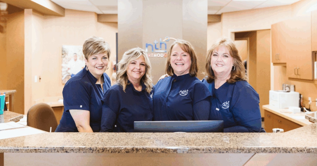 Nth Degree Orthodontics office team, smiling at desk, waiting for you to use your FSA for braces or clear aligners